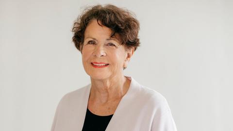 Die Frauen- Finanzberaterin Helma Sick lächelt in die Kamera. Farblich ist alles in hellen, weißlichen Tönen gehalten.