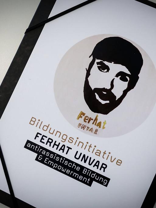 Ein Schild mit der stilisierten Zeichnung des Gesichts eines jungen Mannes. Darunter steht "Bildungsinitiative Ferhat Unvar. Antirassistische Bildung und Empowerment".