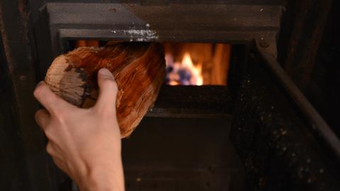 Ein Mann legt ein Stück Holz in einem Kachelofen nach.