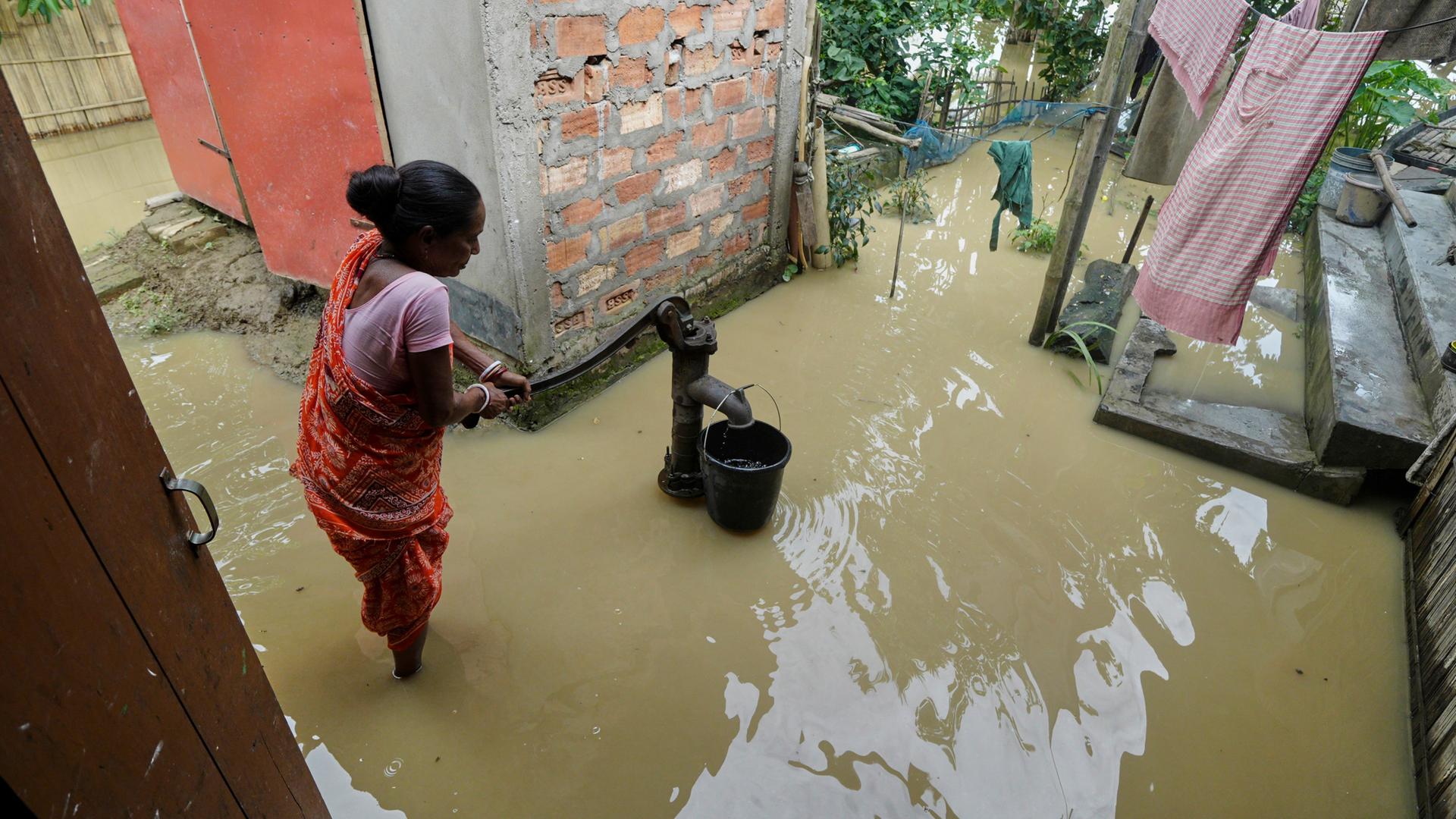 Indien, Kampur: Eine Frau benutzt eine Handpumpe, um Wasser inmitten der überfluteten Umgebung ihres Hauses nach tagelangen sintflutartigen Monsunregenfällen zu sammeln. 
