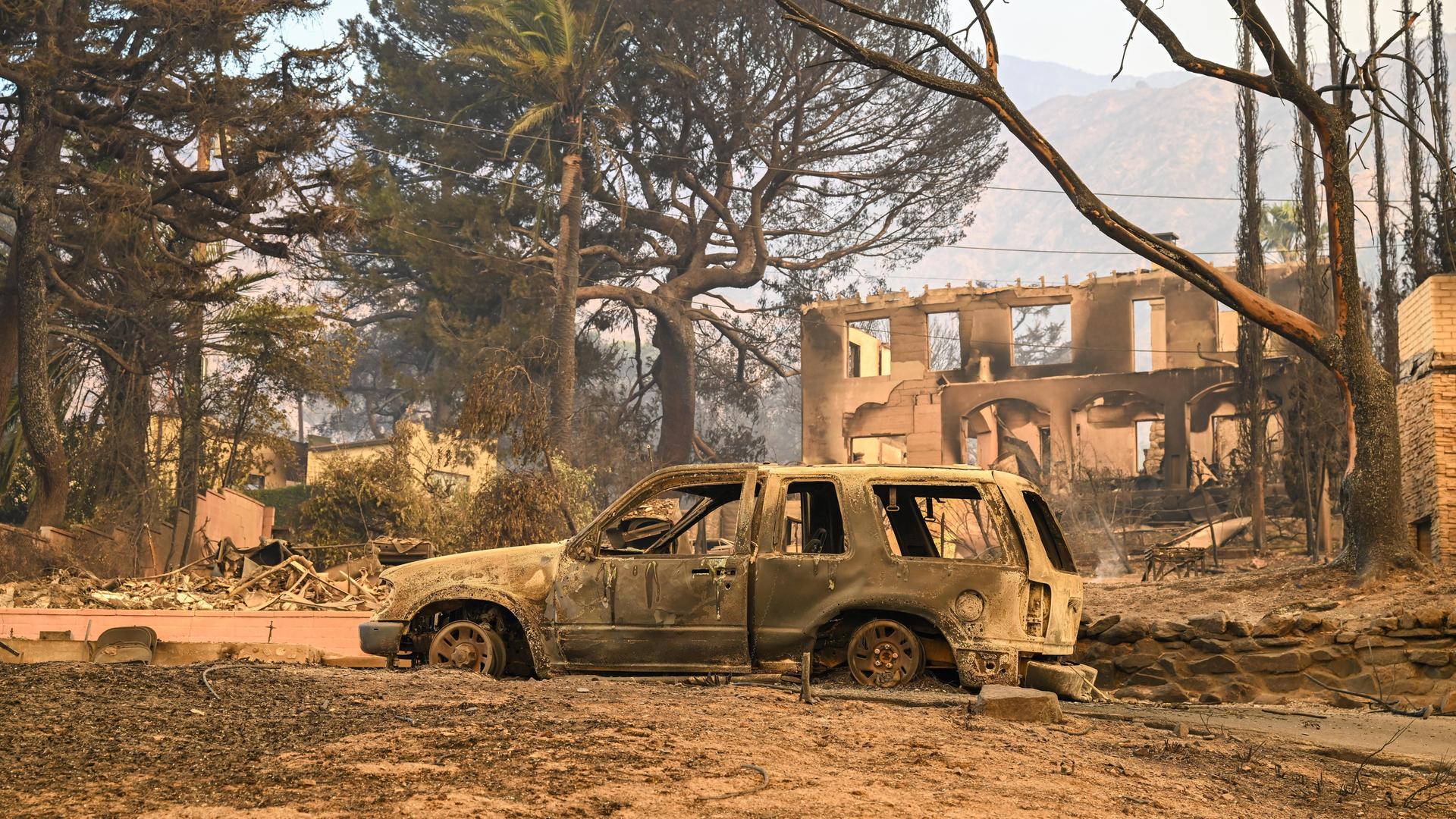 In Los Angeles ist steht ein ausgebranntes Auto inmitten der von Waldbränden zerstörten Umgebung. 