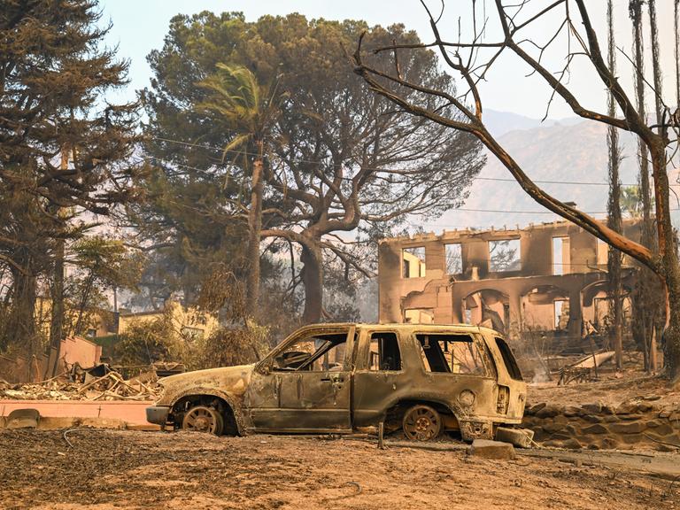 In Los Angeles ist steht ein ausgebranntes Auto inmitten der von Waldbränden zerstörten Umgebung. 