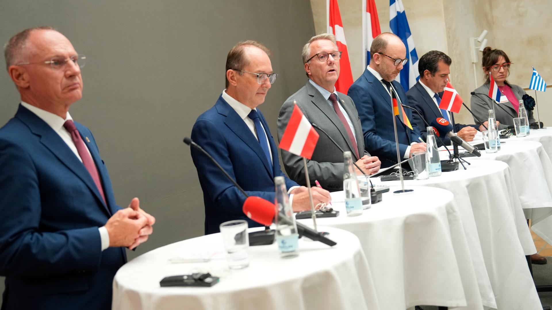 Mehrere Politikerinnen und Politiker stehen nebeneinander an runden Tischen an Mikrofonen und sprechen zu Pressevertreterin Mehrere Politikerinnen und Politiker stehen nebeneinander an runden Tischen an Mikrofonen und sprechen zu Pressevertreterin