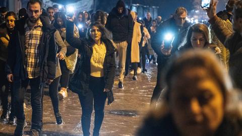 Menschen gehen im strömenden Regen mit Lichtern in den Händen über eine dunkle Straße.