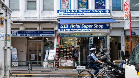 Ein Polizist fährt mit dem Fahrrad an einem Geschäft im Tokioter Stadtviertel Okubo vorbei. Das Banner am Geschäft verät, dass die Inhaber aus Indonesien stammen und Halal Produkte verkaufen.