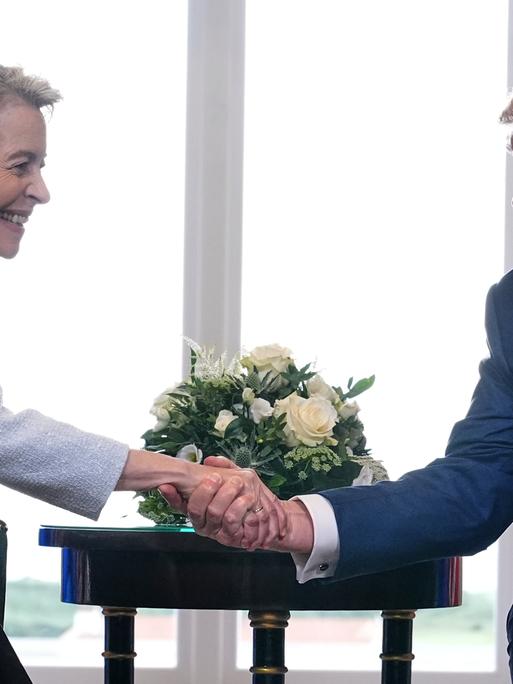 US-Präsident Trump traf die Präsidentin der Europäischen Kommission, von der Leyen, zu Gesprächen in Schottland. Beide schütteln die Hände und lächeln.