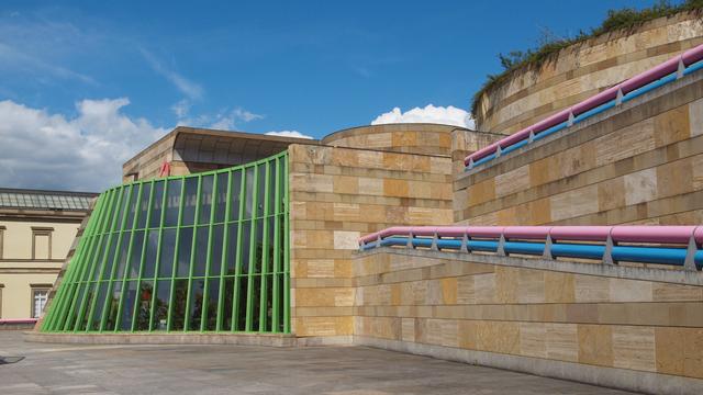 Das sandfarbende Gebäude der Neuen Stuttgarter Staatsgalerie mit rosanen und blauen Umrandungen sowie hellgrünen Fensterstreben