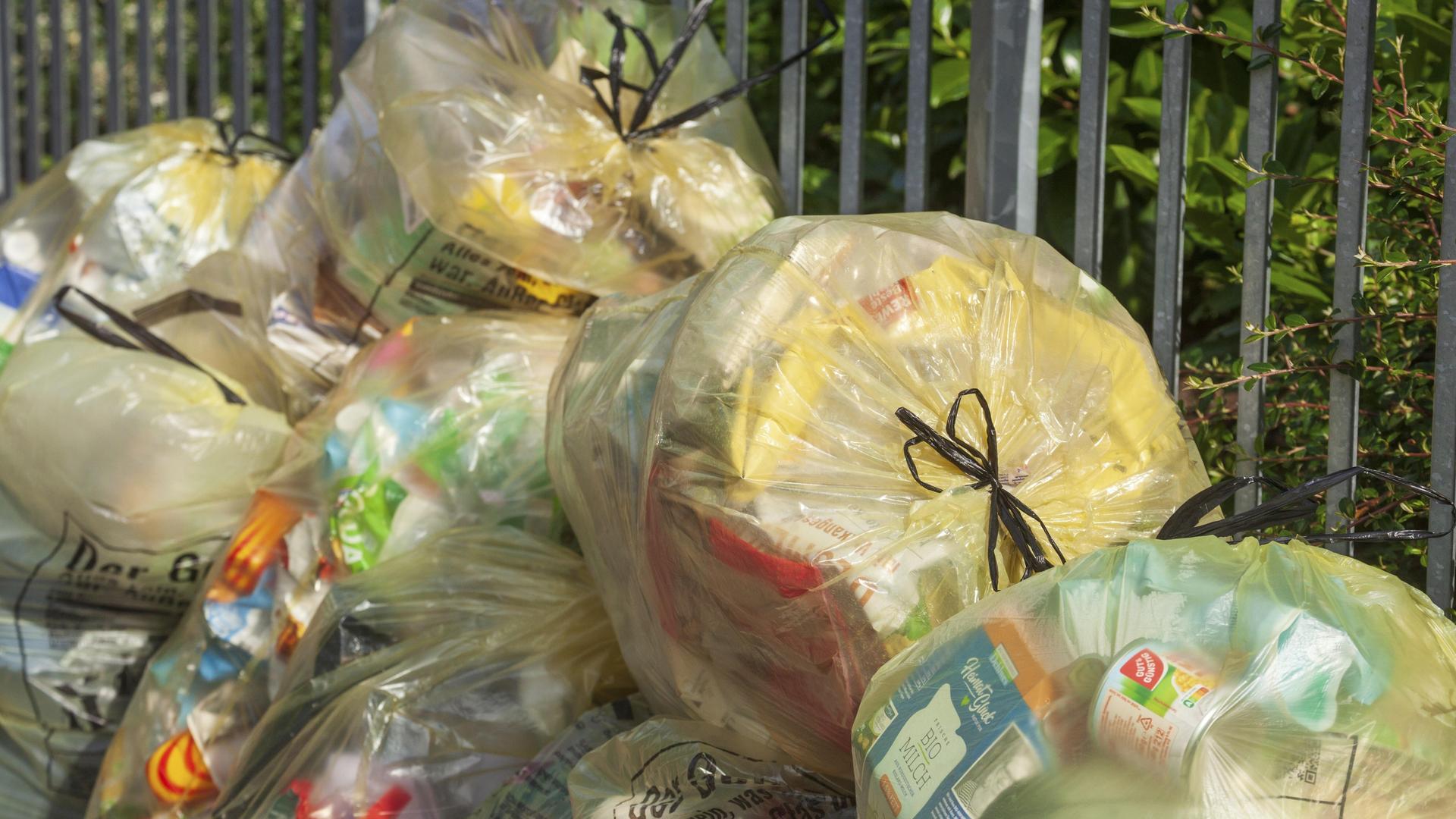 Gelbe Säcke mit Plastikmüll stapeln sich an einer Straße.