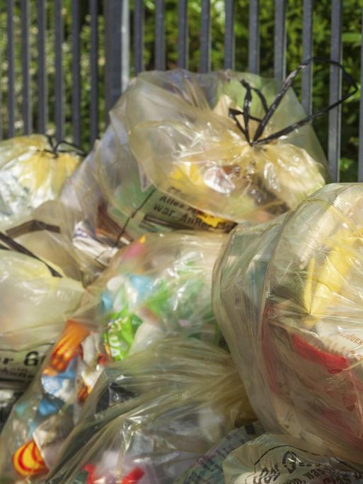 Gelbe Säcke mit Plastikmüll stapeln sich an einer Straße.
