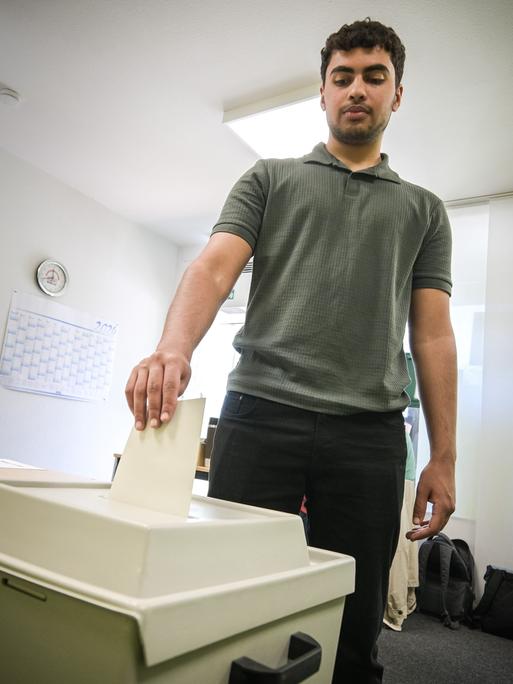 Ein junger Mann steckt einen Briefumschlag in eine Wahlurne.