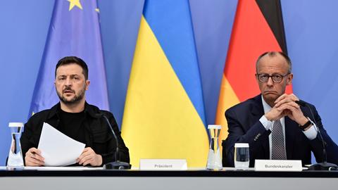 Bundeskanzler Merz und der ukrainische Präsident Selenskyj sitzen nebeneinander und warten auf den Beginn der Videkonferenz.