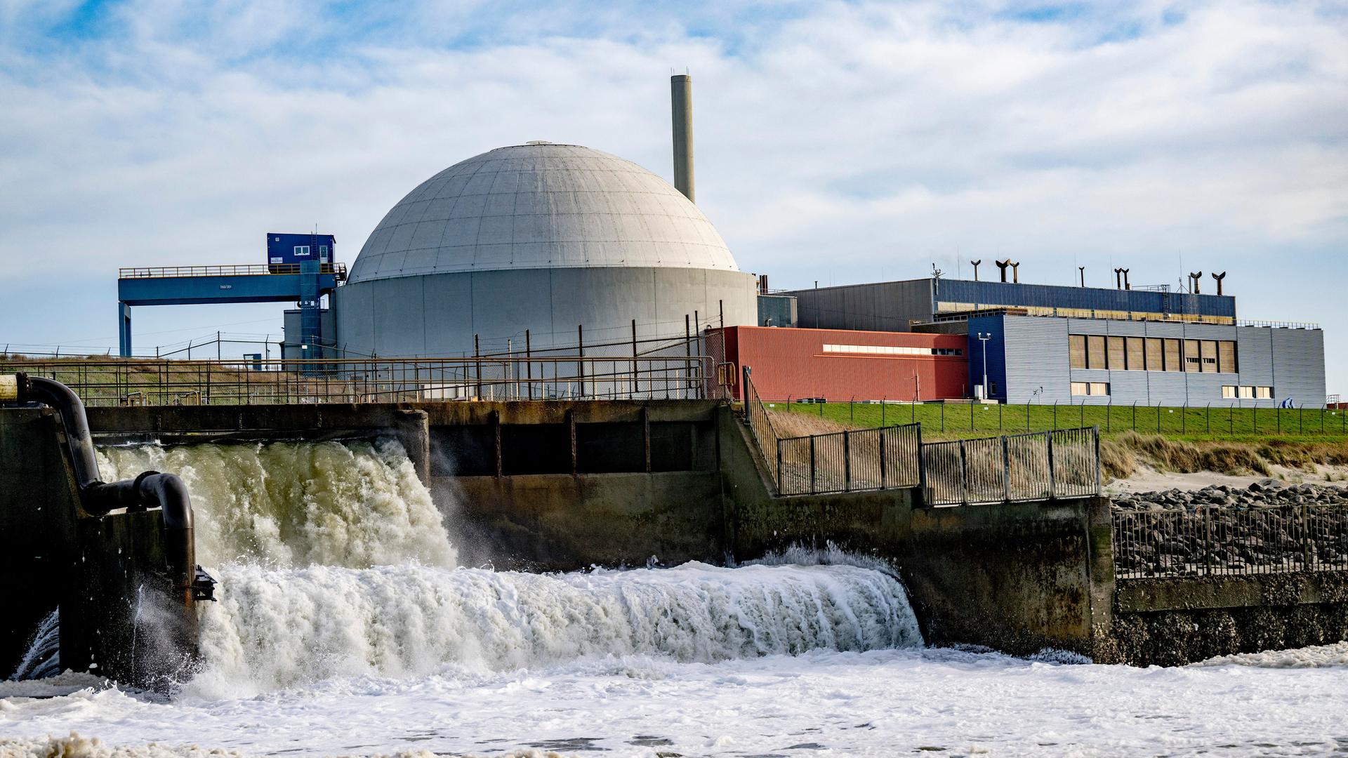Wasser strömt aus einer Öffnung; im Hintergrund ist die Reaktorkuppel des Atomkraftwerks Borssele zu sehen.