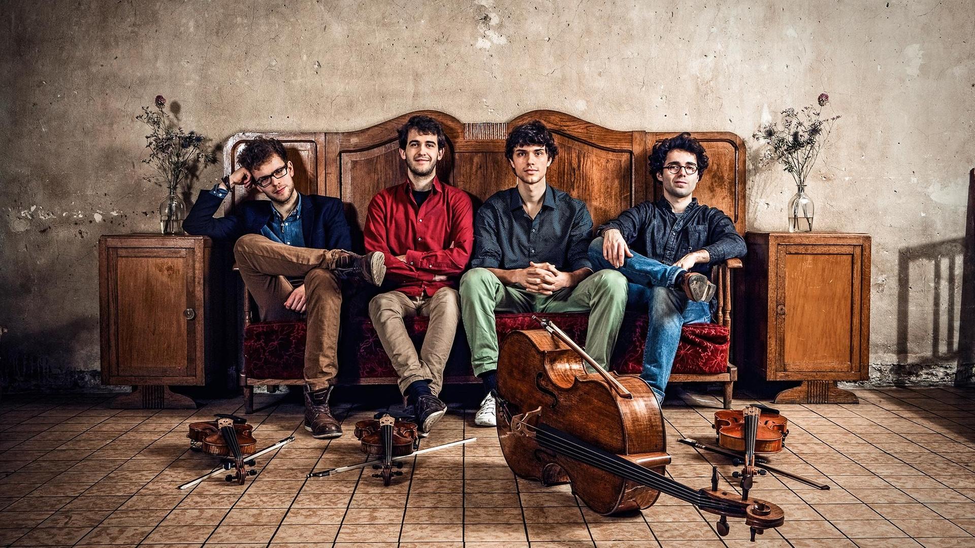 Die Musiker des Vision String Quartet sitzen auf einem Sofa und haben ihre Instrumente vor sich auf den Boden gelegt