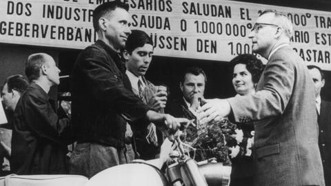 Der millionste Gastarbeiter in der Bundesrepublik, Armando Rodrigues de Sa (l.) aus Portugal, steht neben dem Moped, das er bei seiner Ankunft am 10.09.1964 im Köln-Deutzer Bahnhof geschenkt bekam.