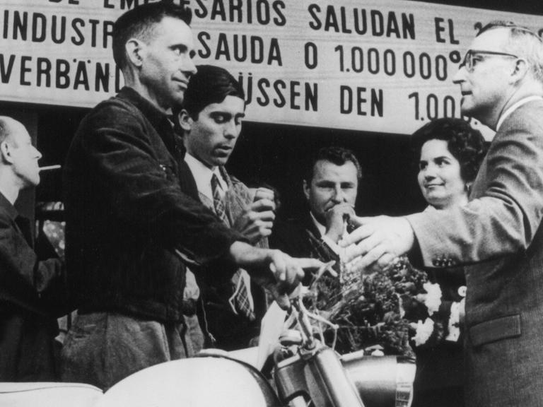 Der millionste Gastarbeiter in der Bundesrepublik, Armando Rodrigues de Sa (l.) aus Portugal, steht neben dem Moped, das er bei seiner Ankunft am 10.09.1964 im Köln-Deutzer Bahnhof geschenkt bekam.