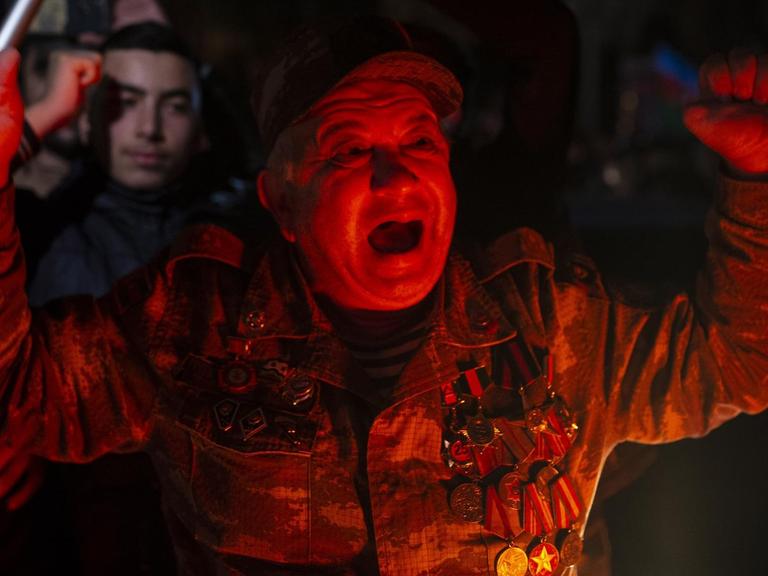 Das Bild zeigt einen Mann mit vielen Orden und rötlicher Beleuchtung beim Jubelschrei. Er feiert am 10. November 2020 in Ganja, Aserbaidschan, die Einigung über die Einstellung der Kämpfe um die Region Berg-Karabach.