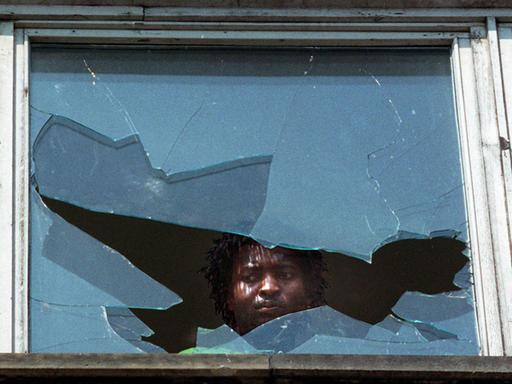 Hoyerswerda: Nachdenklich und betroffen schaut der mocambiquanische Arbeiter durch eine eingeworfene Scheibe des Wohnheinmes. Das Haus war in den letzten Tagen ebenso wie das Asylantenheim Ziel von Anschlägen Rechtsradikaler.