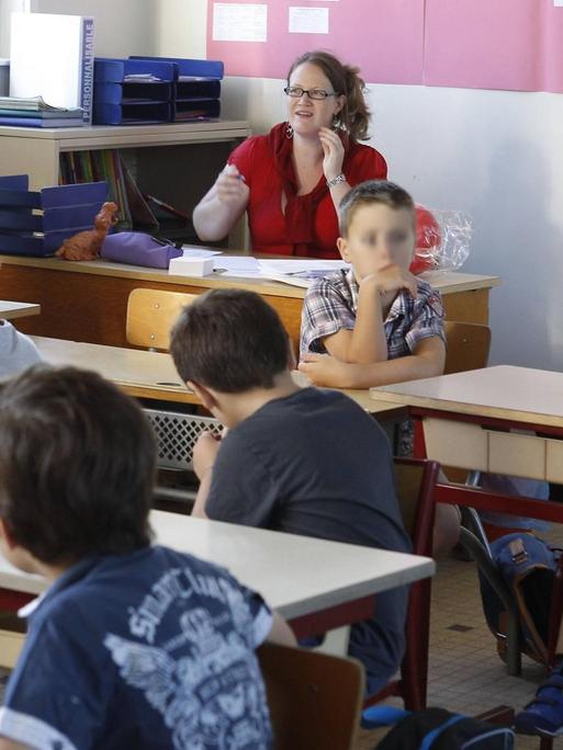 Eine Lehrerin sitzt in Frankreich in einem Klassenzimmer vor ihren Schülern.