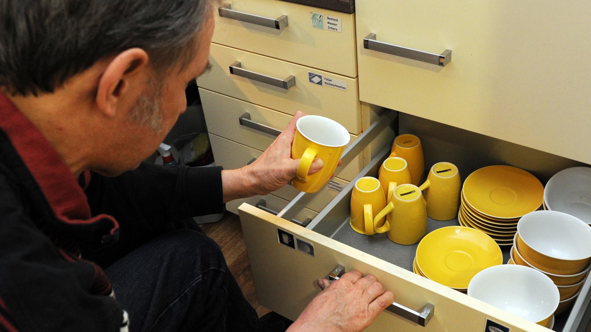 Ein Mann nimmt sich eine gelbe Tasse aus dem Schrank