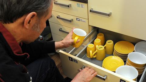 Ein Mann nimmt eine gelbe Tasse aus einer Schublade mit Geschirr.