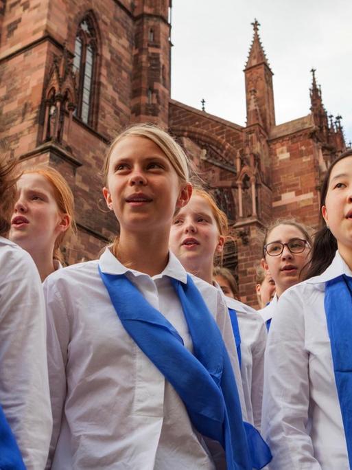 Mädchen mit weißer Bluse und blauem Halstuch vor dem Freiburger Münster.