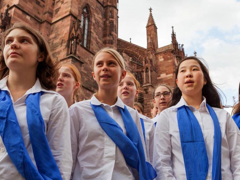 Mädchen mit weißer Bluse und blauem Halstuch vor dem Freiburger Münster.