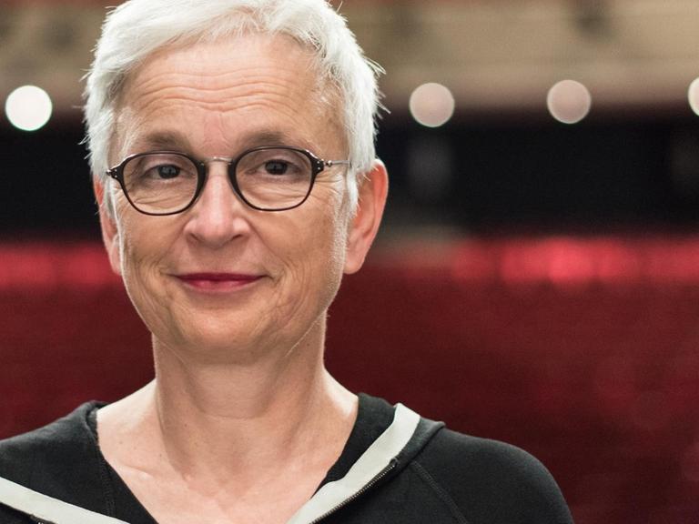Barbara Mundel steht im Theater Freiburg und trägt kurze Haare und eine schwarze Brille