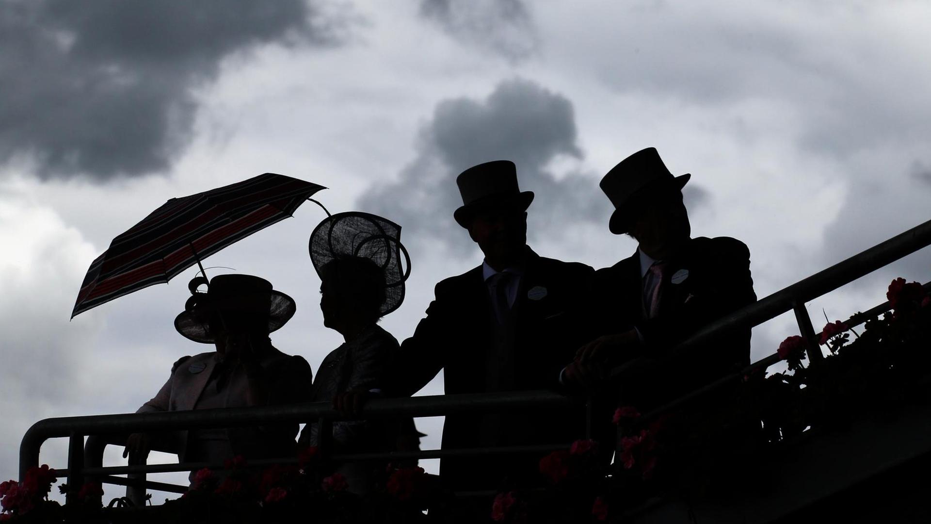 Silhouetten von zwei links stehenden, elegant gekleideten Frauen mit Hut und einem Regenschirm und zwei Männern mit Zylinder rechts daneben vor einem Himmel mit dunklen Wolken