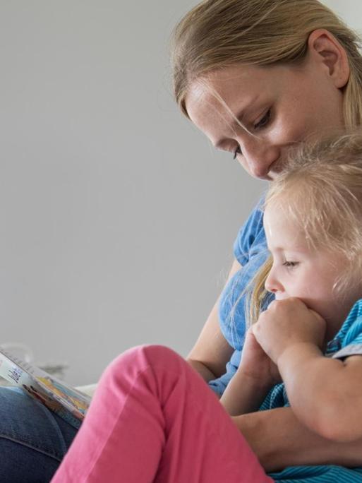 Eine Mutter liest ihrer Tochter auf der Couch etwas vor