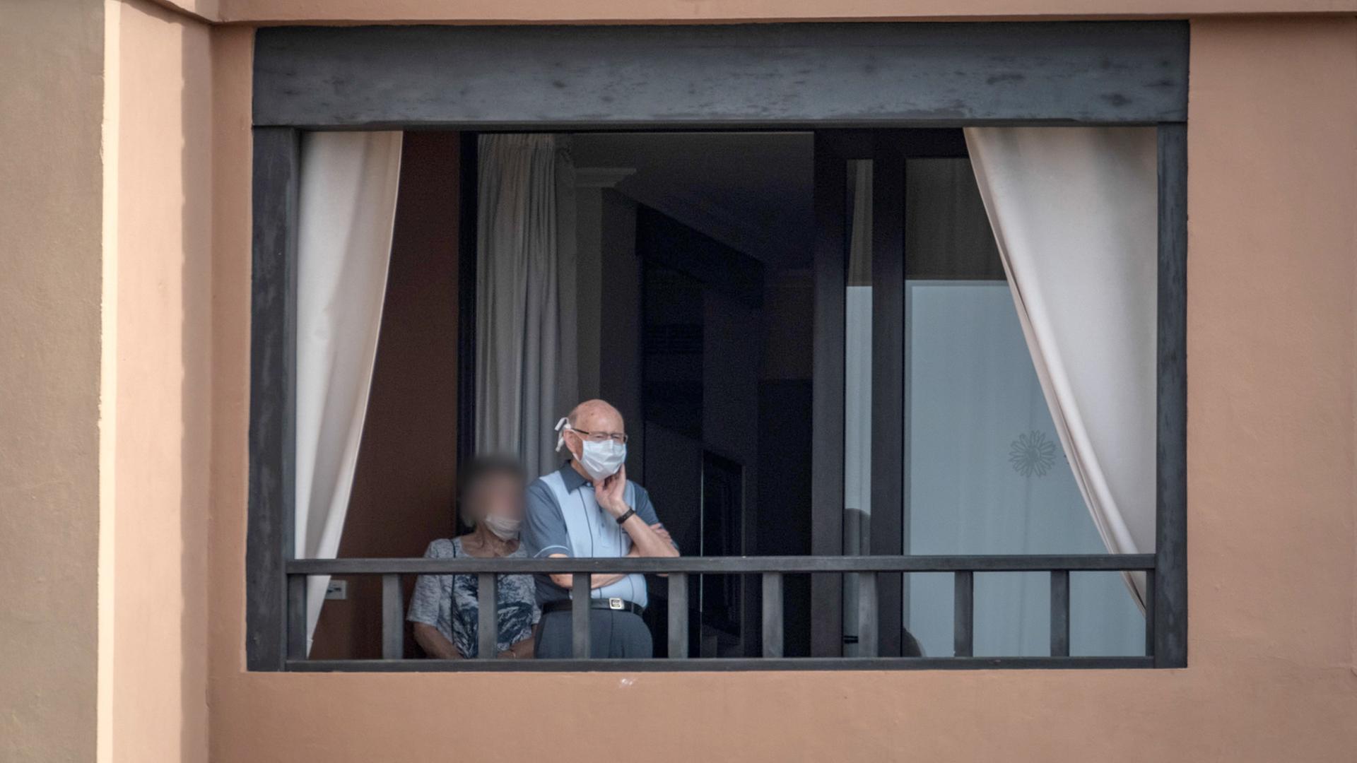 Ältere Leute stehen mit Mundschutz auf einem Balkon des Hotels H10 Costa Adeje Palace.