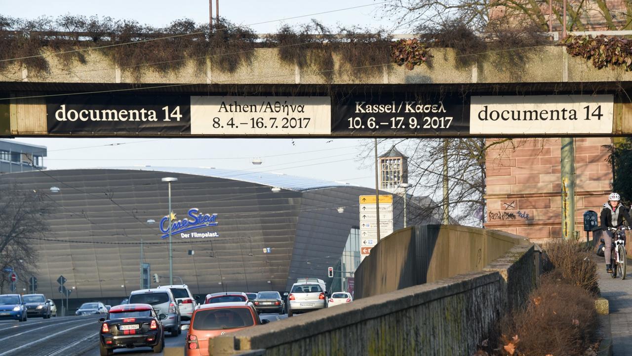 An einer Straßenbrücke hängt ein Werbetransparent für die diesjährige Kunstschau in Athen und Kassel.