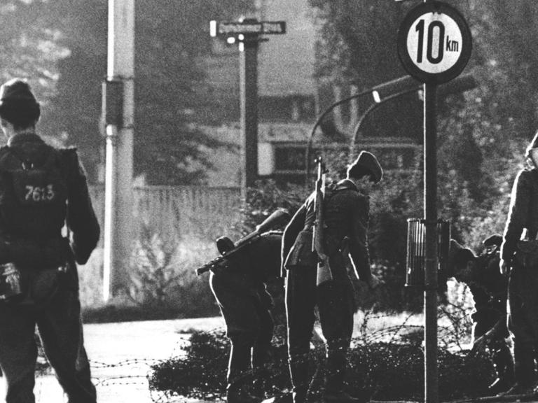 Volkspolizisten beim Errichten von Stacheldrahtsperren am Potsdamer Platz. Am frühen Sonntagmorgen des 13. August 1961 wurde unter der Aufsicht von bewaffneten Streitkräften der DDR mit der Errichtung von Straßensperren aus Stacheldraht und dem Bau einer Mauer begonnen, um den Ostteil Berlins vom Westteil abzusperren. Die Mauer soll den ständig steigenden Flüchtlingsstrom von Ost- nach West-Berlin stoppen.