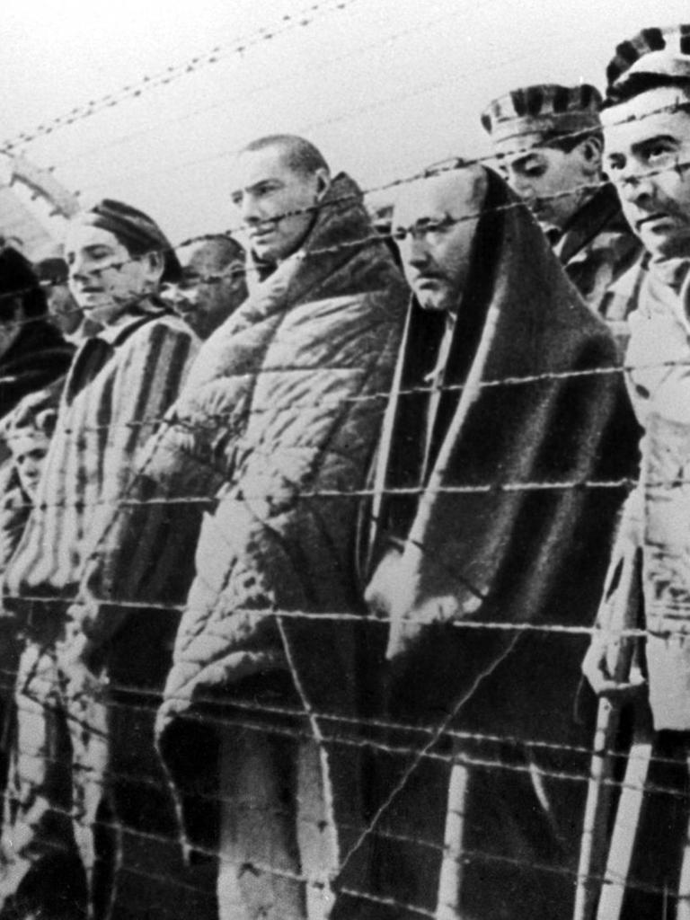 Hinter Stacheldraht stehen Menschen im Vernichtungslager Auschwitz 1945, die Aufnahme ist schwarz-weiß