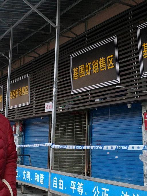 Eine Frau mit Mundschutz steht vor dem geschlossenen Markt in Wuhan.