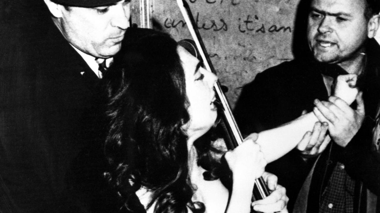 Die Cellistin Charlotte Moorman wird unter Protest von der Polizei abgeführt, weil sie ohne Oberbekleidung ein Konzert in einem kleinen Off-Broadway-Theater gegeben hat. Auf dem Programm stand "Melodie-Elegie des Erinnyes" von Jules Massenet.