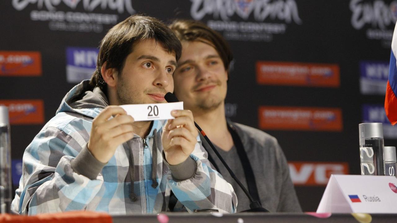 Pjotr Nalitsch sitzt bei einer Pressekonferenz zum Eurovision Song Contest 2010 an einem Tisch und zeigt seine Startnummer zwanzig.  