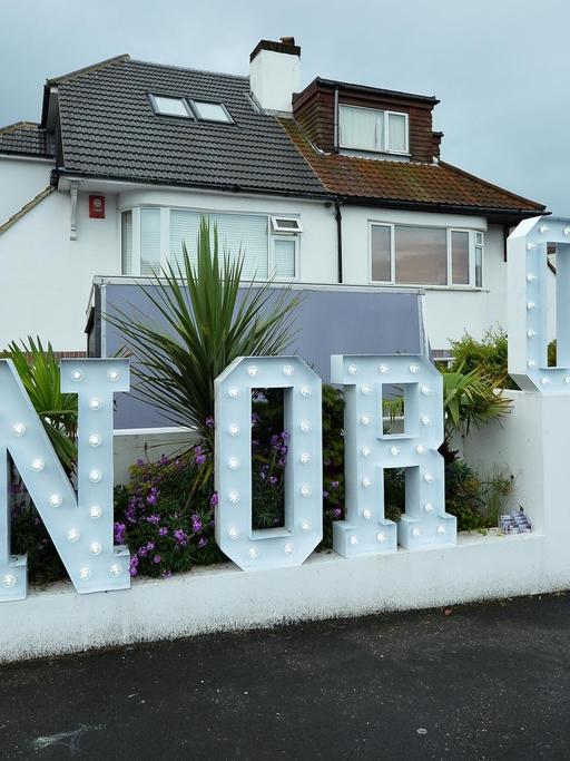 Ein beleuchteter "In or Out"-Schriftzug vor einem Haus.