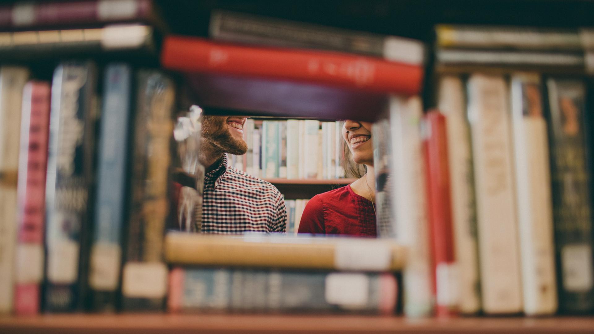 Ein Mann und eine Frau stehen zwischen Bücherregalen und lächeln sich an.