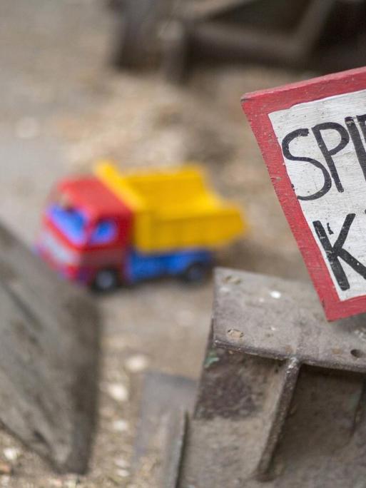 Ein Schild mit der Aufschrift "Spielende Kinder" an einem Spielplatz, im Hintergrund ein Spielzeug-LKW