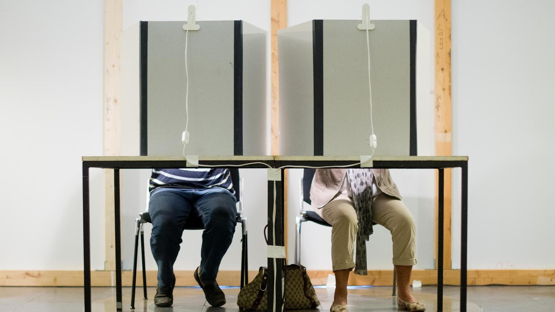 Ein Mann und eine Frau sitzen in einem Wahlraum und füllen ihre Stimmzettel aus