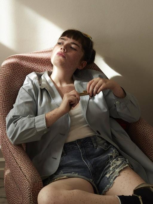 Eine Teenagerin sitzt in einem Sessel und sieht gelangweilt aus (Symbolfoto)