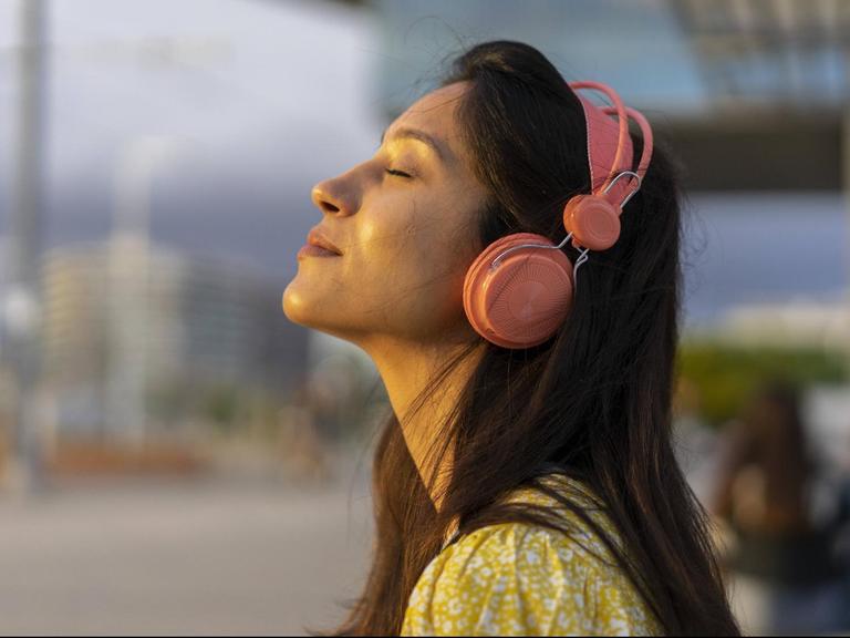 Eine junge Frau mit Kopfhörern und geschlossenen Augen scheint in entspannter Stimmung zu sein