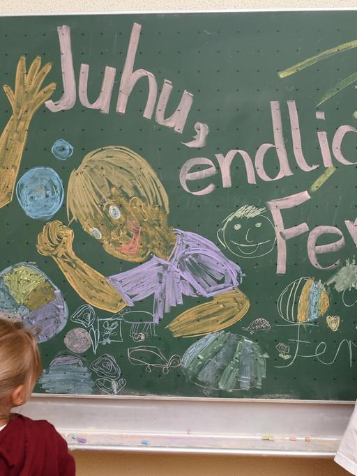Erst- und Zweitklässler malen am 29.07.2015 in der Grundschule in Weißenau (Baden-Württemberg) bei Ravensburg am letzten Schultag des Jahres für den Fotografen ein Bild an die Tafel, auf dem "Juhu, endlich Ferien", zu lesen ist.