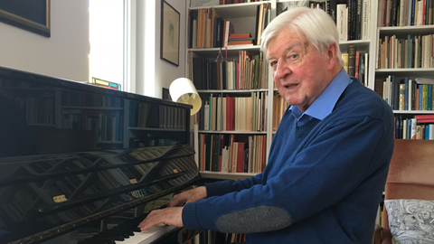 Hans Maier sitzt am Klavier, im Hintergrund eine Bücherwand.