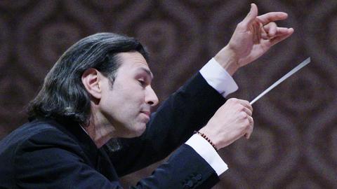 Der Dirigent im Profil, beide Hände für das Orchester erhoben.