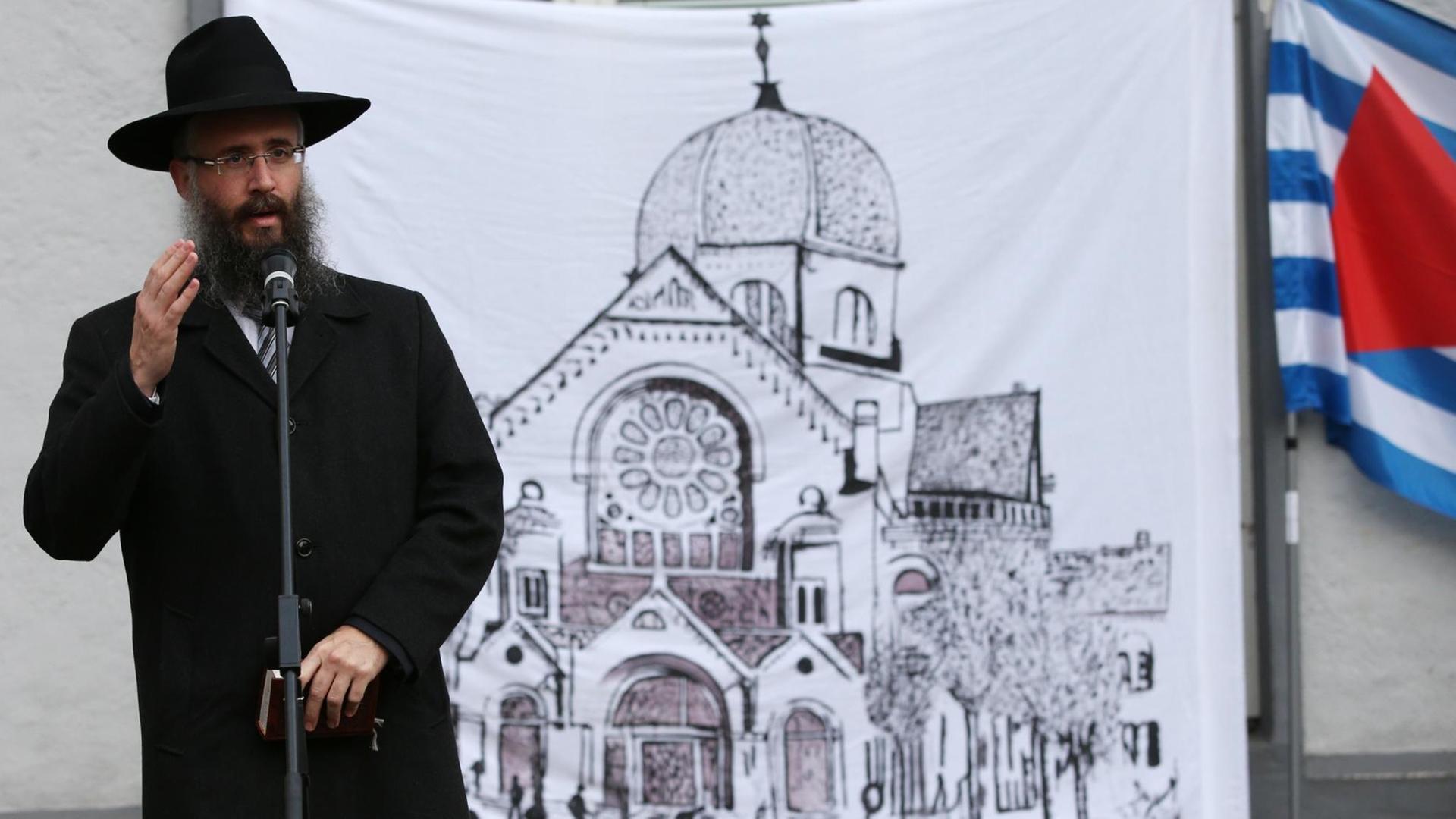 Hamburgs Landesrabbiner Shlomo Bistritzky steht vor einem Transparent mit einer Zeichnung der Bornplatz-Synagoge.
