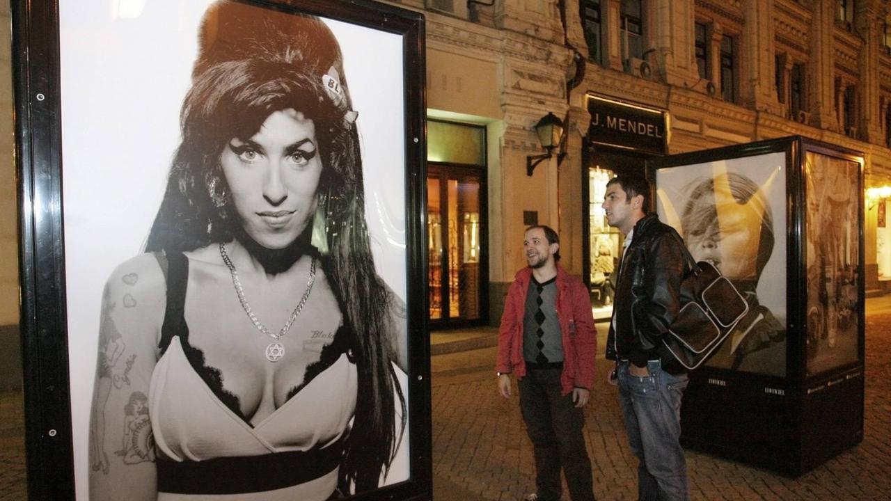 Zwei Passanten stehen vor einem Schaukasten, in dem ein Porträt von Amy Winehouse gezeigt wird.