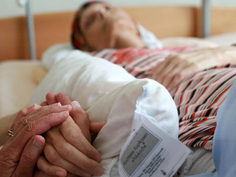 Eine ehrenamtliche Helferin hält die Hand einer sterbenden Bewohnerin, die in ihrem Bett im Christophorus Hospiz in München liegt.