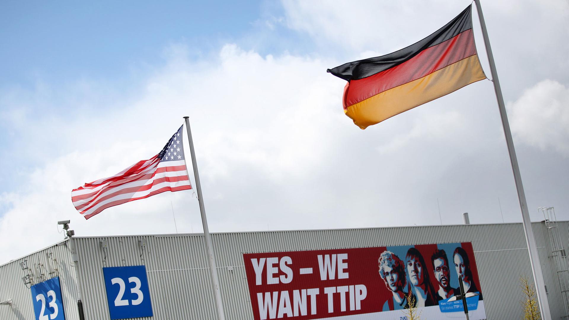 Eine amerikanische Flagge und eine deutsche Flagge wehen am 24.04.2016 auf dem Gelände der Hannover Messe in Hannover (Niedersachsen) vor einem Plakat mit der Aufschrift "Yes - We want TTIP". Die weltgrößte Industriemesse Hannover Messe wird am 24. April von US-Präsident Obama eröffnet. Partnerland der Messe sind in diesem Jahr die USA.