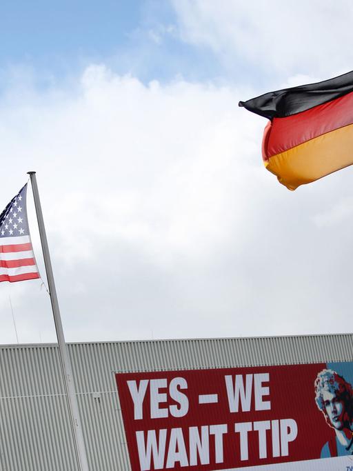 Eine amerikanische Flagge und eine deutsche Flagge wehen am 24.04.2016 auf dem Gelände der Hannover Messe in Hannover (Niedersachsen) vor einem Plakat mit der Aufschrift "Yes - We want TTIP". Die weltgrößte Industriemesse Hannover Messe wird am 24. April von US-Präsident Obama eröffnet. Partnerland der Messe sind in diesem Jahr die USA.